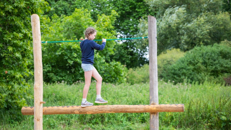 A girl playing on a balance beam in the 'Wild Play' area, Mottisfont, Hampshire